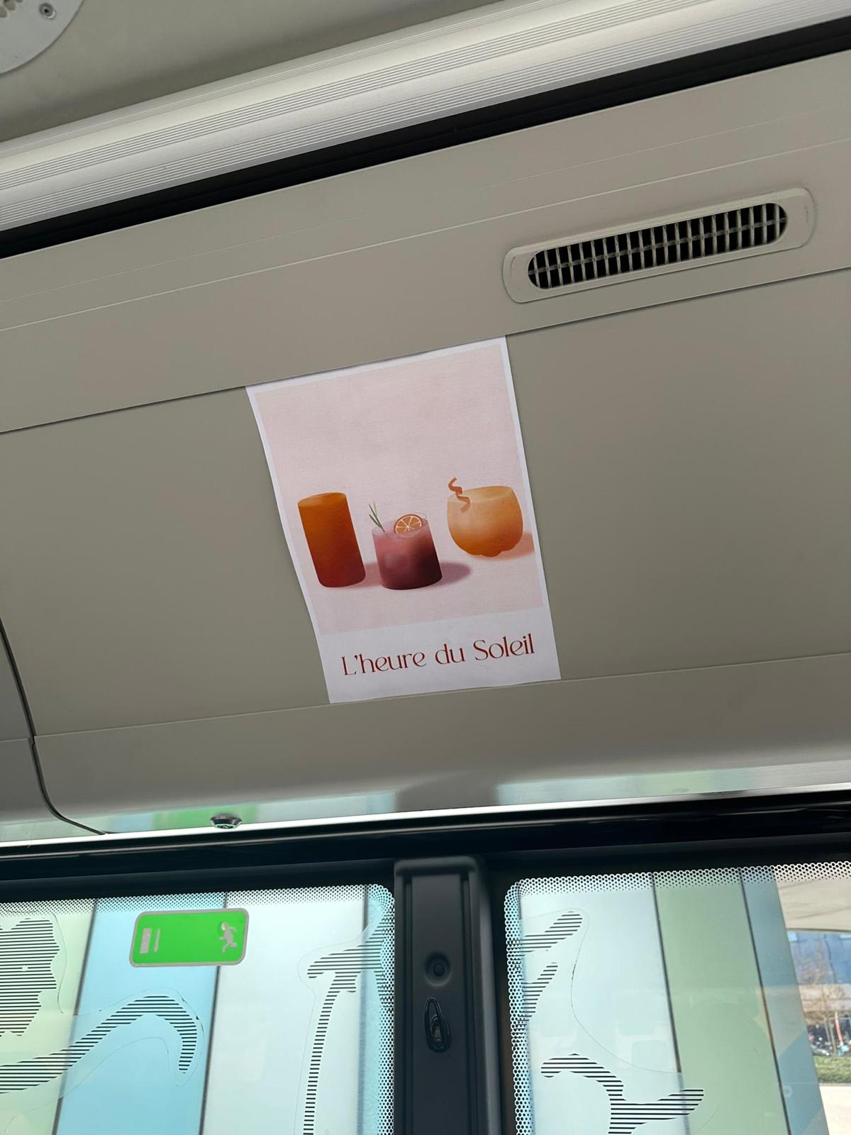 Een roze poster met zomerse cocktails en de tekst 'L'heure de soleil' hangt in een bus boven de toegangsdeuren. 