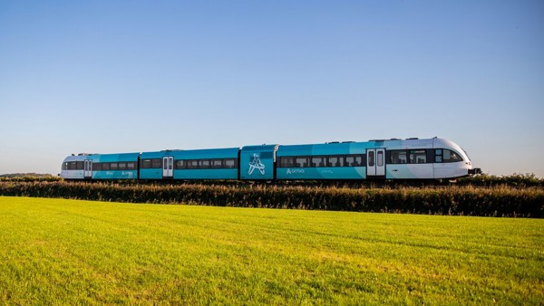 Een blauw-witte Arriva-trein rijdt door een groen landschap onder een blauwe lucht.