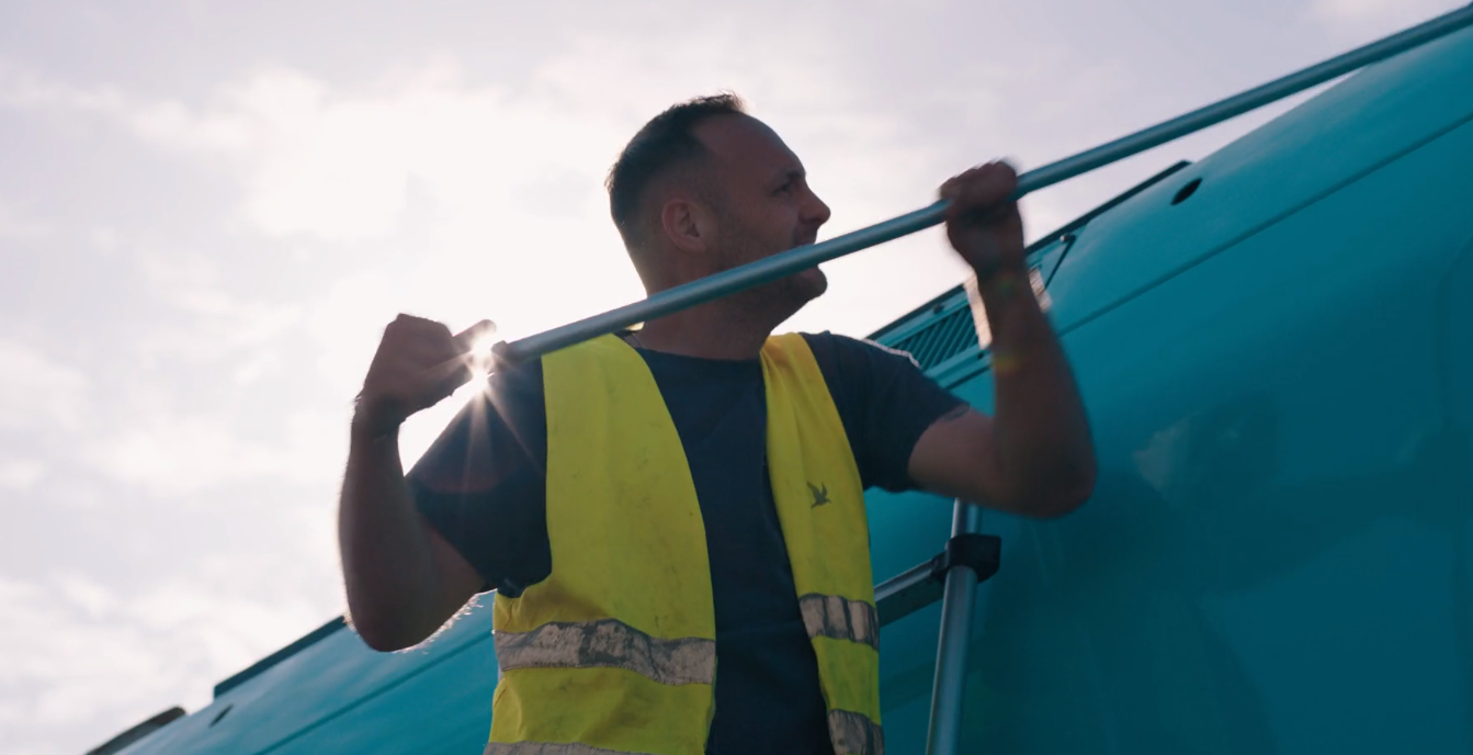 Een man poetst een blauwe Arriva trein onder de stralende zon.