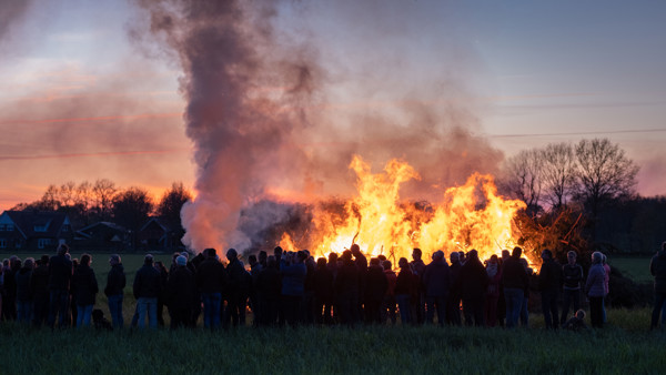 een schemeravond waar je een aangestoken paasvuur ziet met rook en een groep mensen om het vuur heen een schemeravond waar je een aangestoken paasvuur ziet met rook en een groep mensen om het vuur heen