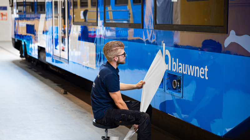 Man is geeft in een werkplaats de buitenkant van de trein nieuwe Blauwnet stickers. Man is geeft in een werkplaats de buitenkant van de trein nieuwe Blauwnet stickers.