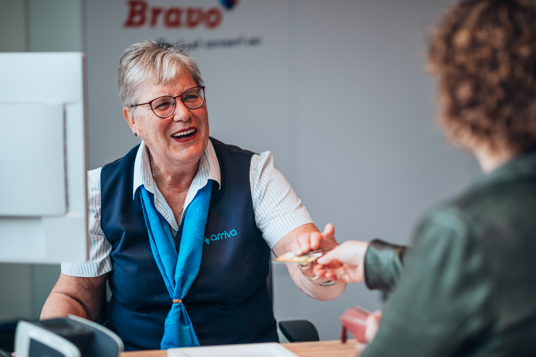 Een lachende service medewerker van Arriva in Tilburg overhandigt een klant haar OV-chipkaart terug.