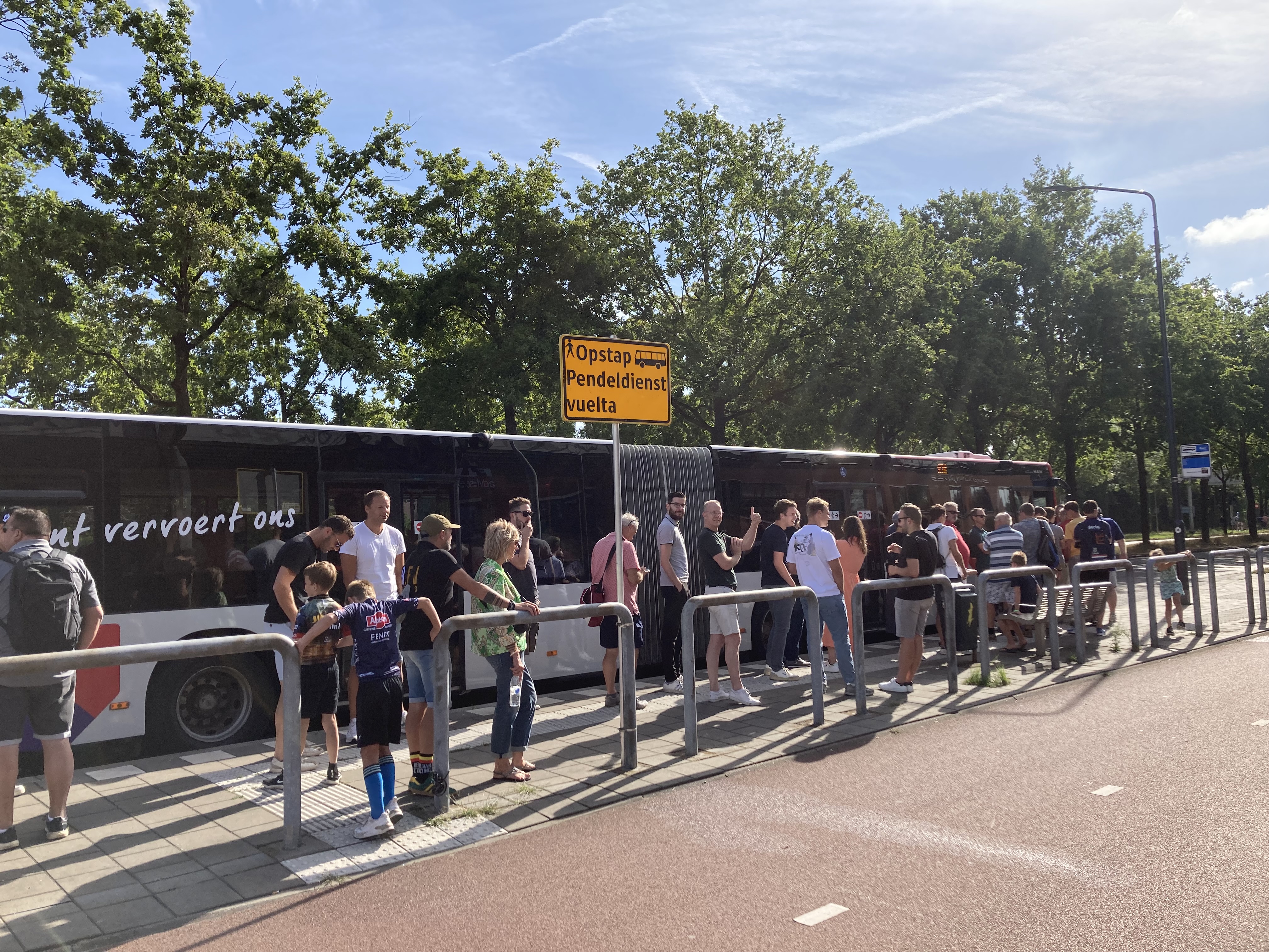 Mensen staan te wachten om in te stappen in een pendeldienst naar de Vuelta. De zon schijnt.