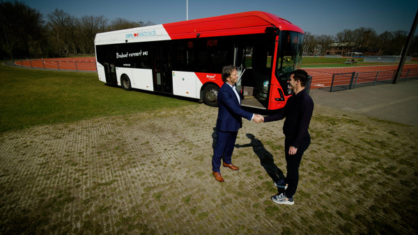 Twee mannen schudden elkaar de hand voor een rood-witte Arriva-bus.