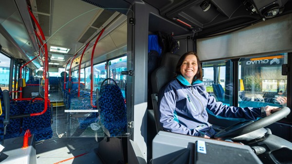 Een vrouwelijke buschauffeur met bruin haar zit achter het stuur van een Arriva-bus en glimlacht. Een vrouwelijke buschauffeur met bruin haar zit achter het stuur van een Arriva-bus en glimlacht.