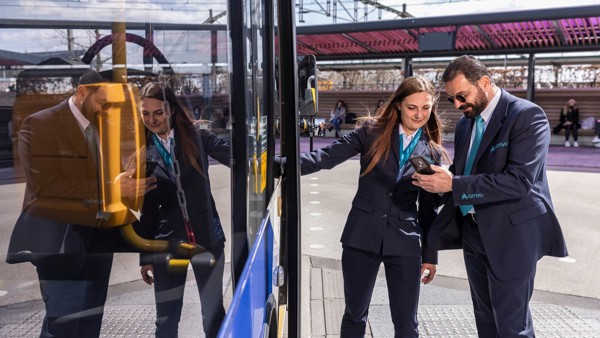 Een mannelijke en vrouwelijke busschauffeur staan naast de bus en kijken samen op een telefoon.