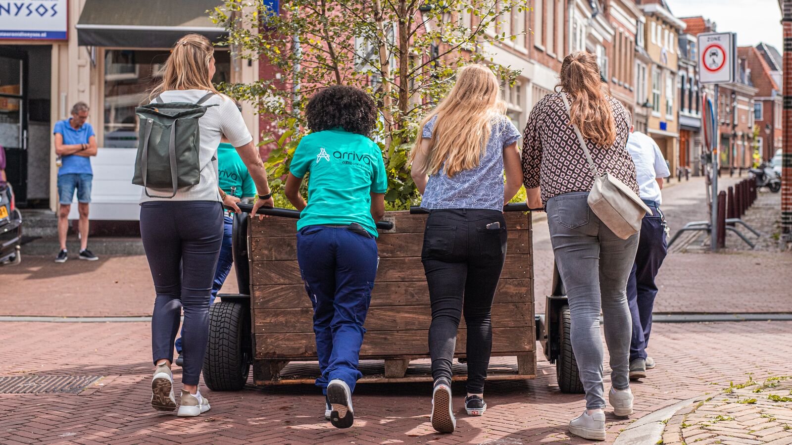Zes vrouwen duwen een kar met daarin bomen over straat.