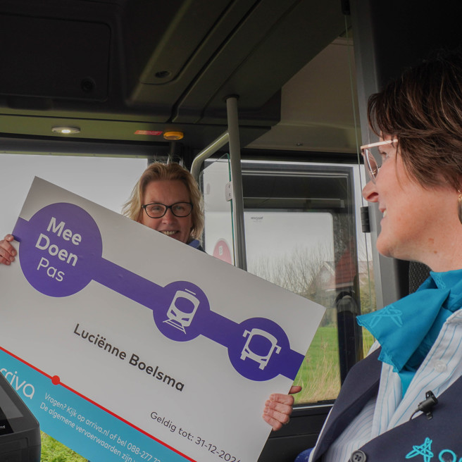 Wethouder van gemeente De Fryske Marren laat een vergrootte Meedoen Pas zien aan een chauffeur van Arriva in de bus