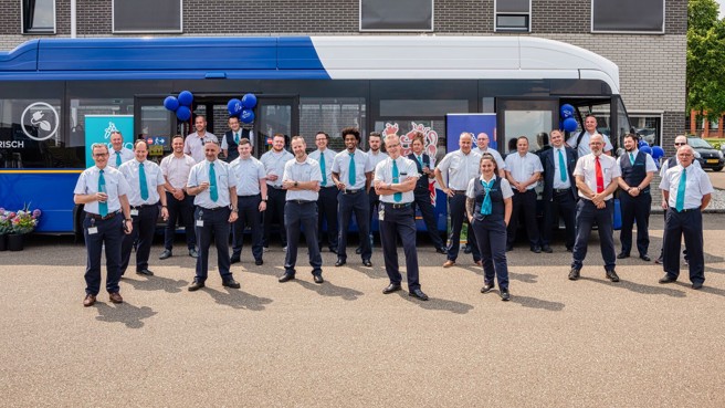 Een grote groep mensen in Arriva-uniform staat trots voor een blauw-witte Arriva-bus met ballonnen eraan.