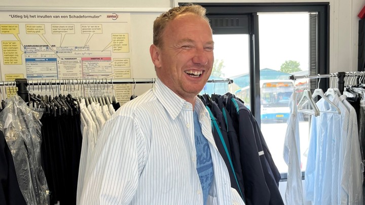 Een lachende man past voor een kledingrek met overhemden een Arriva-uniform. Een lachende man past voor een kledingrek met overhemden een Arriva-uniform.