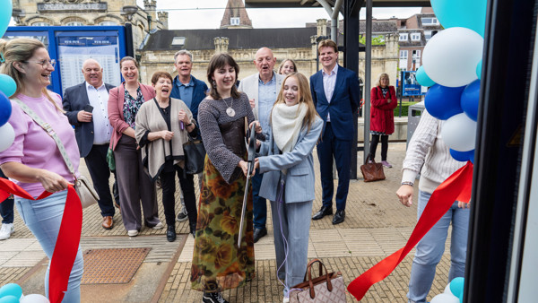 op het perron in Valkenburg staat een vrolijk lachende groep mensen. In het midden staan zangeres Emma Kok en woordkunstenaar Eline Willaert en knippen officieel het lint door op het perron in Valkenburg staat een vrolijk lachende groep mensen. In het midden staan zangeres Emma Kok en woordkunstenaar Eline Willaert en knippen officieel het lint door
