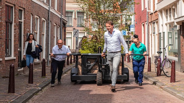 Drie personen trekker een kar met daarin bomen over straat.