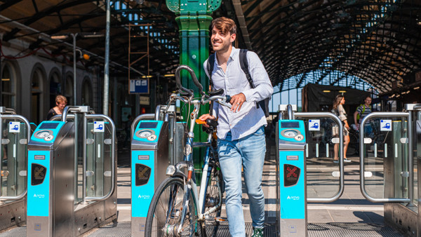 Een man loopt met zijn fiets door de ov-poortjes op een station.