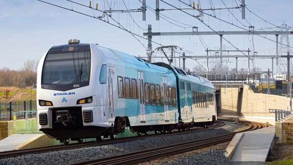 Een blauw-witte Arriva-trein rijdt over het spoor onder een blauwe lucht.