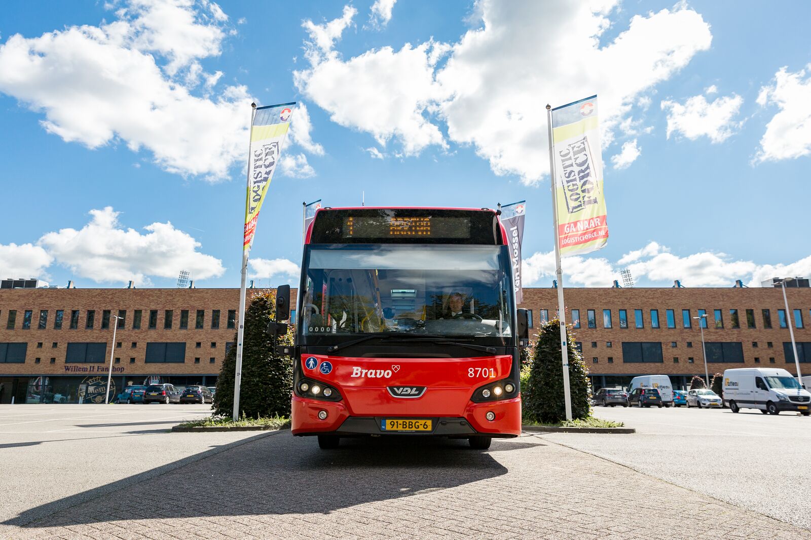De voorkant van een rode bus van Arriva is te zien terwijl die geparkeerd staat, met de chauffeur achter het stuur.