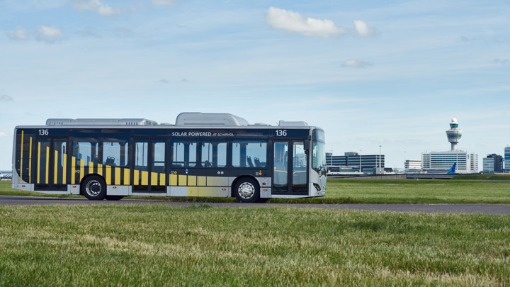 Elektrische Arriva-bus rijdt door een weiland onder een blauwe lucht met wolken. Op de achtergrond is Schiphol te zien. Elektrische Arriva-bus rijdt door een weiland onder een blauwe lucht met wolken. Op de achtergrond is Schiphol te zien.