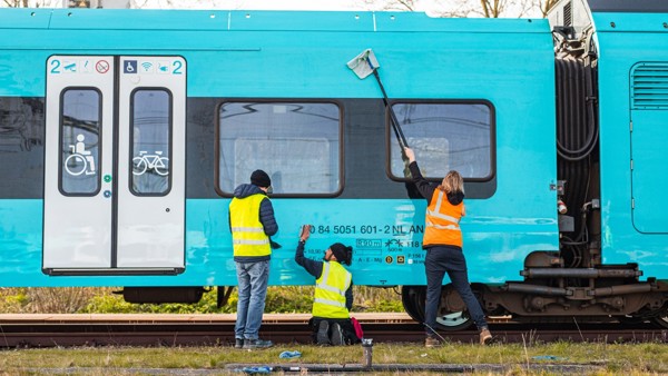 Drie mensen maken een blauwe Arriva-trein schoon.