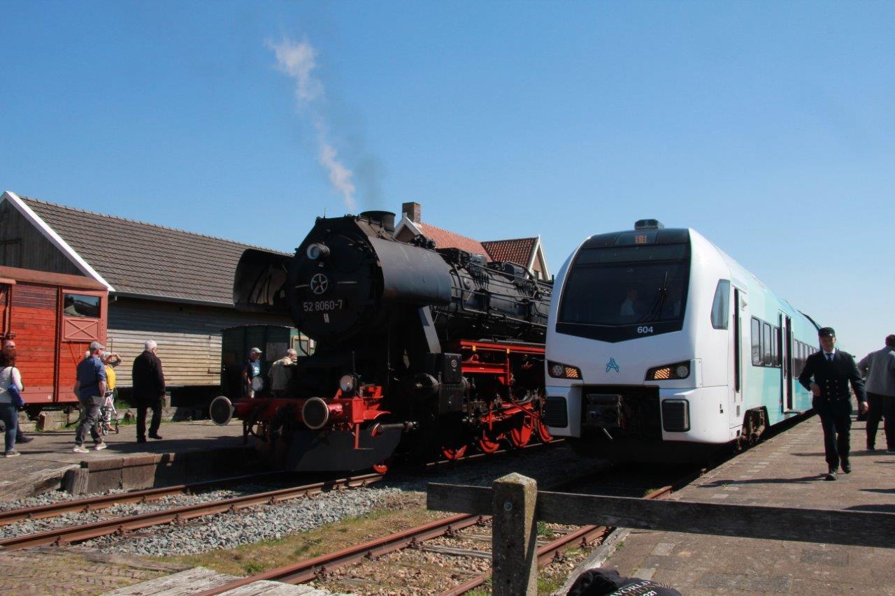 Een historische zwarte locomotief staat naast een moderne blauw-witte Arriva-trein.