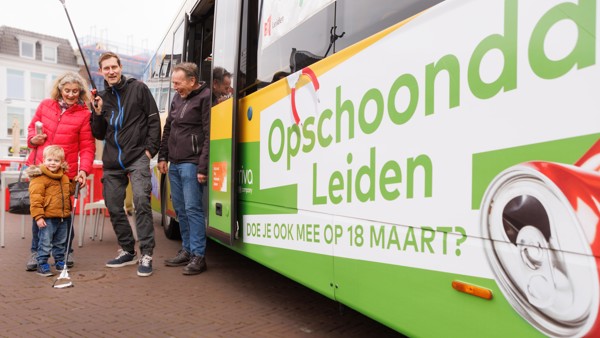 Een groep mensen van verschillende leeftijden staat naast een Arriva-bus. Een man met een afvalprikker lacht terwijl hij poseert.