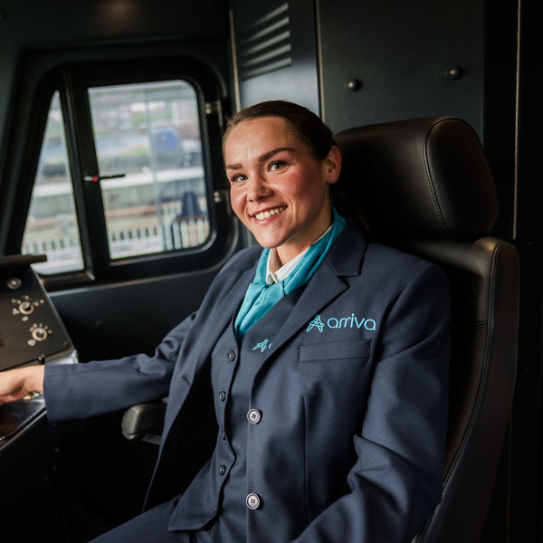 Een lachende machinist in Arriva-uniform zit in de bestuurderscabine van een trein en kijkt naar de camera. Een lachende machinist in Arriva-uniform zit in de bestuurderscabine van een trein en kijkt naar de camera.