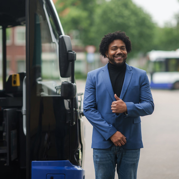 Een teammanager van Arriva in blauw pak staat lachend naast een bus. Een teammanager van Arriva in blauw pak staat lachend naast een bus.