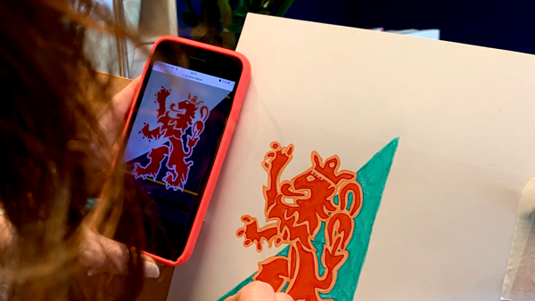 Vrouw tekent leeuw van Limburg na van haar telefoon. Op de achtergrond staat een plant.