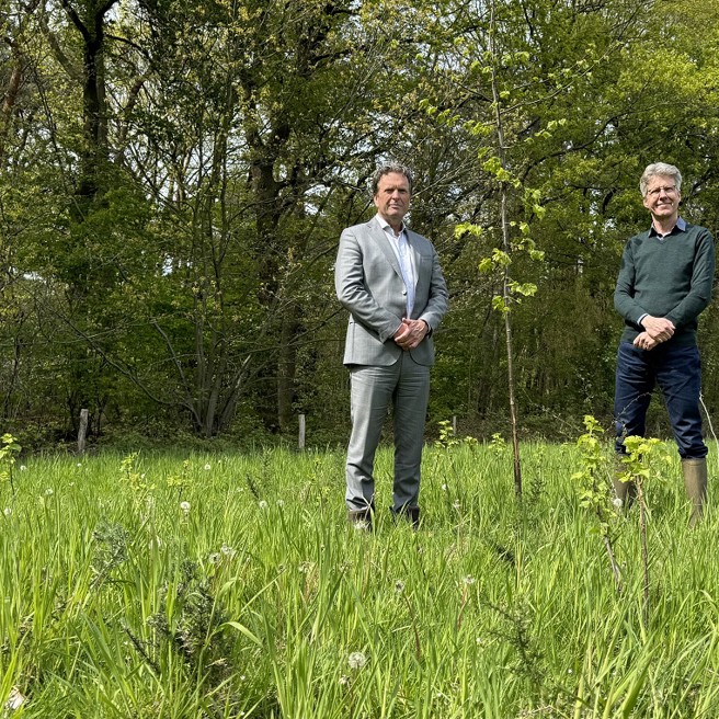 Arriva-directeur Jan Pieter Been staat bij een jong aangeplant boompje op een veld vol wilde groene bergroeiing. Aan de andere kant van het boompje staat Joris Hogenboom, directeur bij Brabants Landschap.