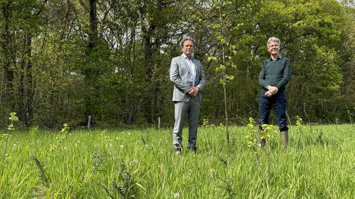 Arriva-directeur Jan Pieter Been staat bij een jong aangeplant boompje op een veld vol wilde groene bergroeiing. Aan de andere kant van het boompje staat Joris Hogenboom, directeur bij Brabants Landschap.