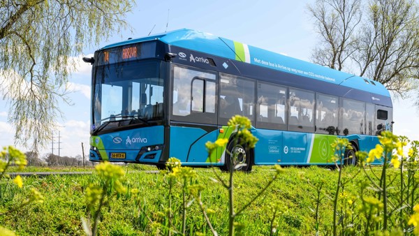 Een blauwe Arriva-waterstofbus rijdt over de weg in een groene omgeving.