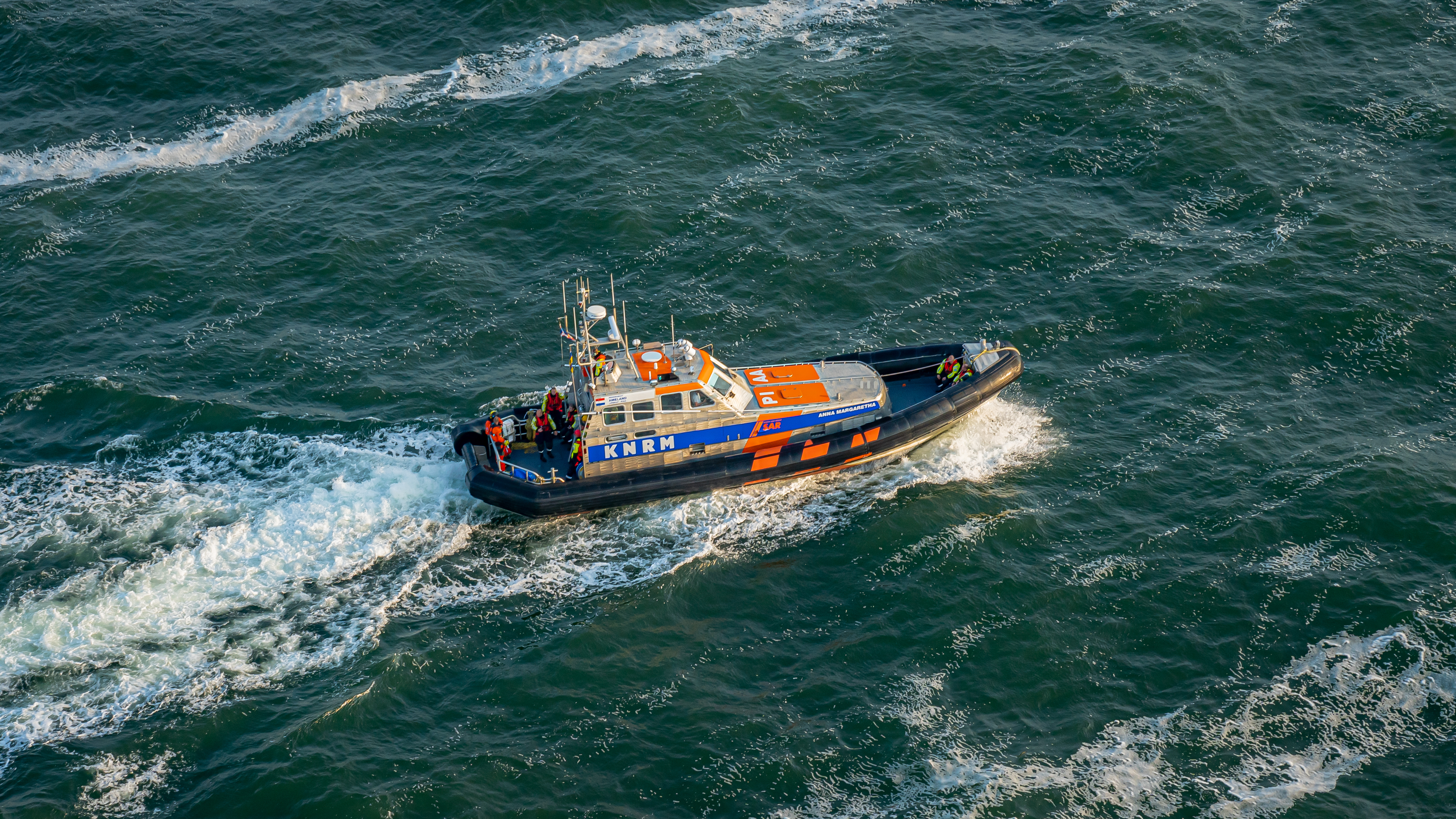 Blauw- witte reddingsboot  met neonoranje accenten van de Koninklijke Nederlandse Reddings Maatschappij  vaart op volle zee