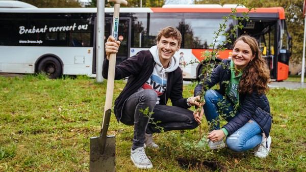 Twee jonge mensen planten een boom, op de achtergrond staat een Arriva-bus.