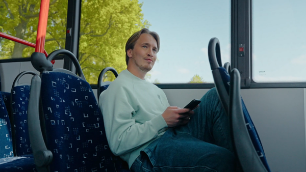 Rapper Snelle zit in een Arriva-bus met zijn telefoon in zijn hand.