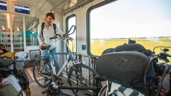 Een man staat met een fiets in een Arriva-trein. Om hem heen staat bagage. Een man staat met een fiets in een Arriva-trein. Om hem heen staat bagage.