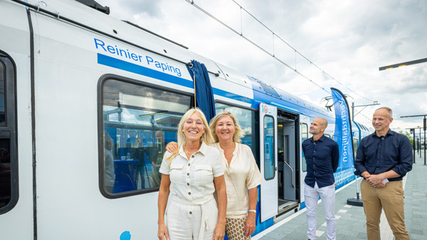 Twee vrouwen en twee mannen staan voor een blauw-witte Arriva-trein met daarop de tekst "Reinier Paping".