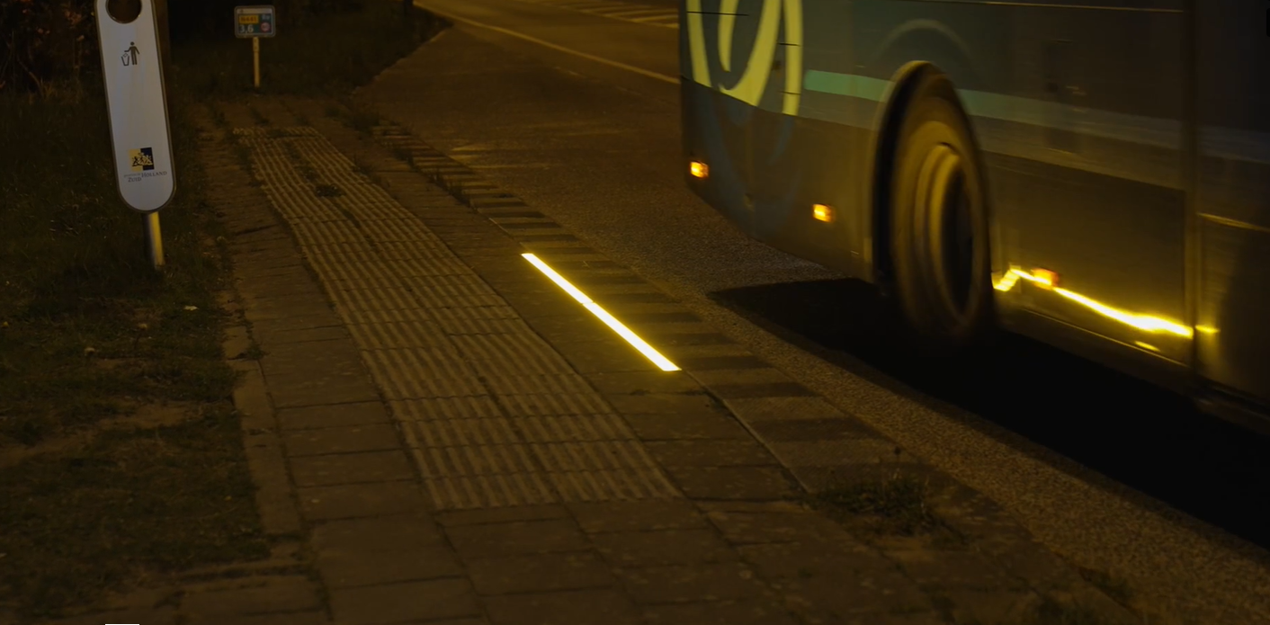 Een strip LED-verlichting op de tegels bij een bushalte in het donker.