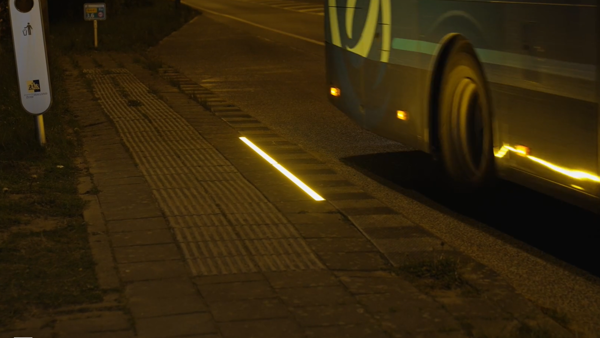 Een strip LED-verlichting op de tegels bij een bushalte in het donker.