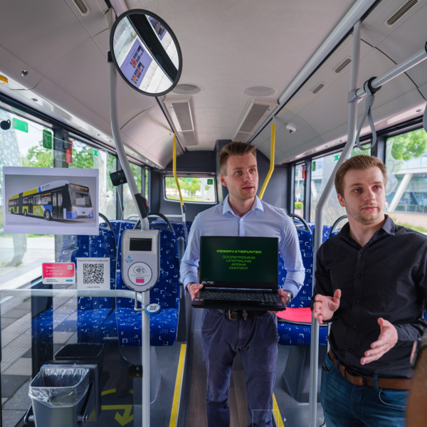 wee mannen in een Arrivabus, één met een laptop waarop ‘Observatiepunten’ staat, en een afbeelding van een elektrische bus op de achtergrond wee mannen in een Arrivabus, één met een laptop waarop ‘Observatiepunten’ staat, en een afbeelding van een elektrische bus op de achtergrond