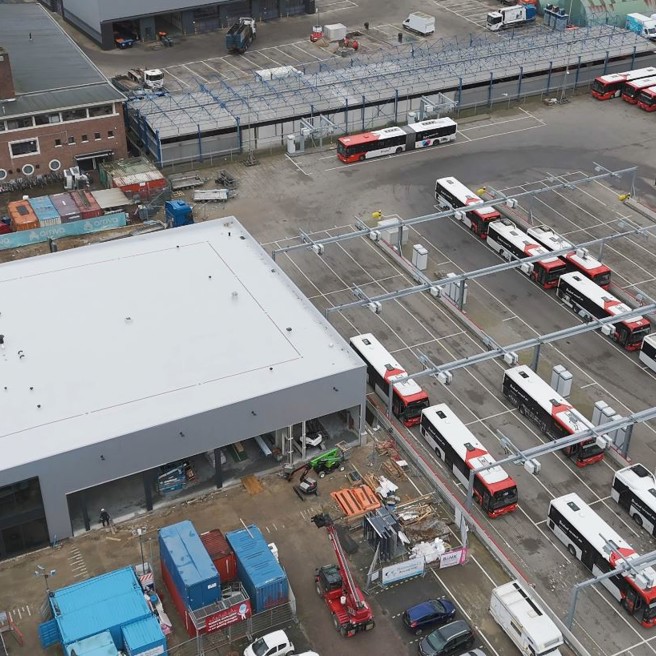 Bovenaanzicht van een vierkant gebouw (werkplaats Tilburg) met rechts daarvan een stuk of 10 bravo bussen bij laadinfra.