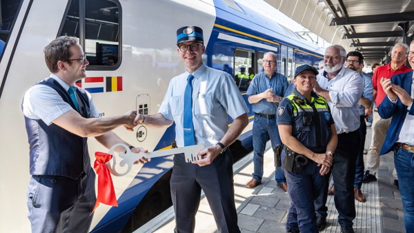 De symbolische sleuteloverdracht tussen Arriva en NMBS treinpersoneel markeert de start van de Drielandentrein. Voor een blauwwitte Arriva Drielandentrein zien we een ceremoniële sleuteloverdracht om de start van de nieuwe treindienst te markeren.