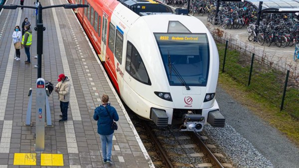 Een bovenaanzicht van een rood-witte Arriva-trein langs het perron, met in de verte een fietsenstalling en gebouwen. Een bovenaanzicht van een rood-witte Arriva-trein langs het perron, met in de verte een fietsenstalling en gebouwen.
