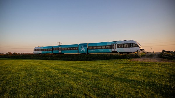 Een blauwe Arriva-trein rijdt door een groen landschap onder een strakblauwe lucht vlak voor zonsopkomst. Een blauwe Arriva-trein rijdt door een groen landschap onder een strakblauwe lucht vlak voor zonsopkomst.