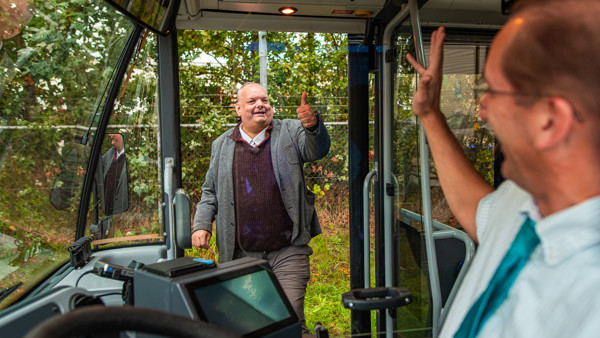 Buschauffeur staat met bus bij halte en zwaait naar reiziger die buiten staat en een duim omhoud houdt. Buschauffeur staat met bus bij halte en zwaait naar reiziger die buiten staat en een duim omhoud houdt.