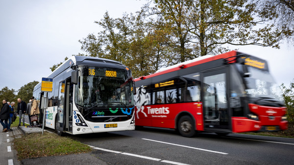 Een witte Arriva-bus met Rrreis erop staat bij de halte en wordt ingehaald door een rode Arriva-bus. Een witte Arriva-bus met Rrreis erop staat bij de halte en wordt ingehaald door een rode Arriva-bus.