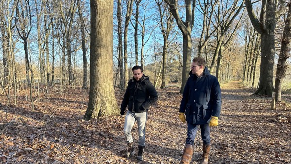 Twee mannen lopen op een zonnige dag door het bos.