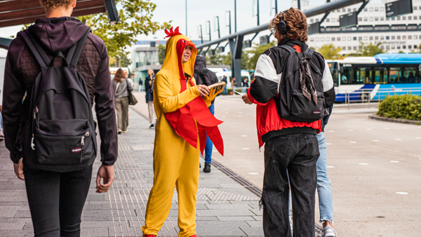 Iemand verkleed als een kip deelt flyers uit bij een busstation. Iemand verkleed als een kip deelt flyers uit bij een busstation.